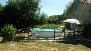 A swimming pool surrounded by a wooden fence, with a white umbrella and chairs nearby. - Fortified Farm 10 Berth Dormitory (La Forêt-sur-Sèvre)