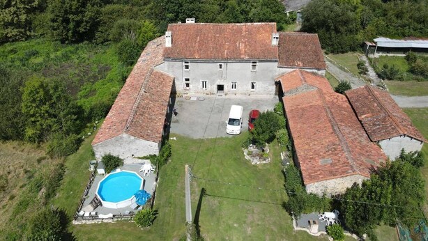 A large, rectangular building with a tiled roof, surrounded by lush greenery and a swimming pool. - Fortified Farm 10 Berth Dormitory (La Forêt-sur-Sèvre)