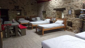 A rustic room with four wooden beds, a small table with a red cloth, and a stone wall. - Fortified Farm 10 Berth Dormitory (La Forêt-sur-Sèvre)