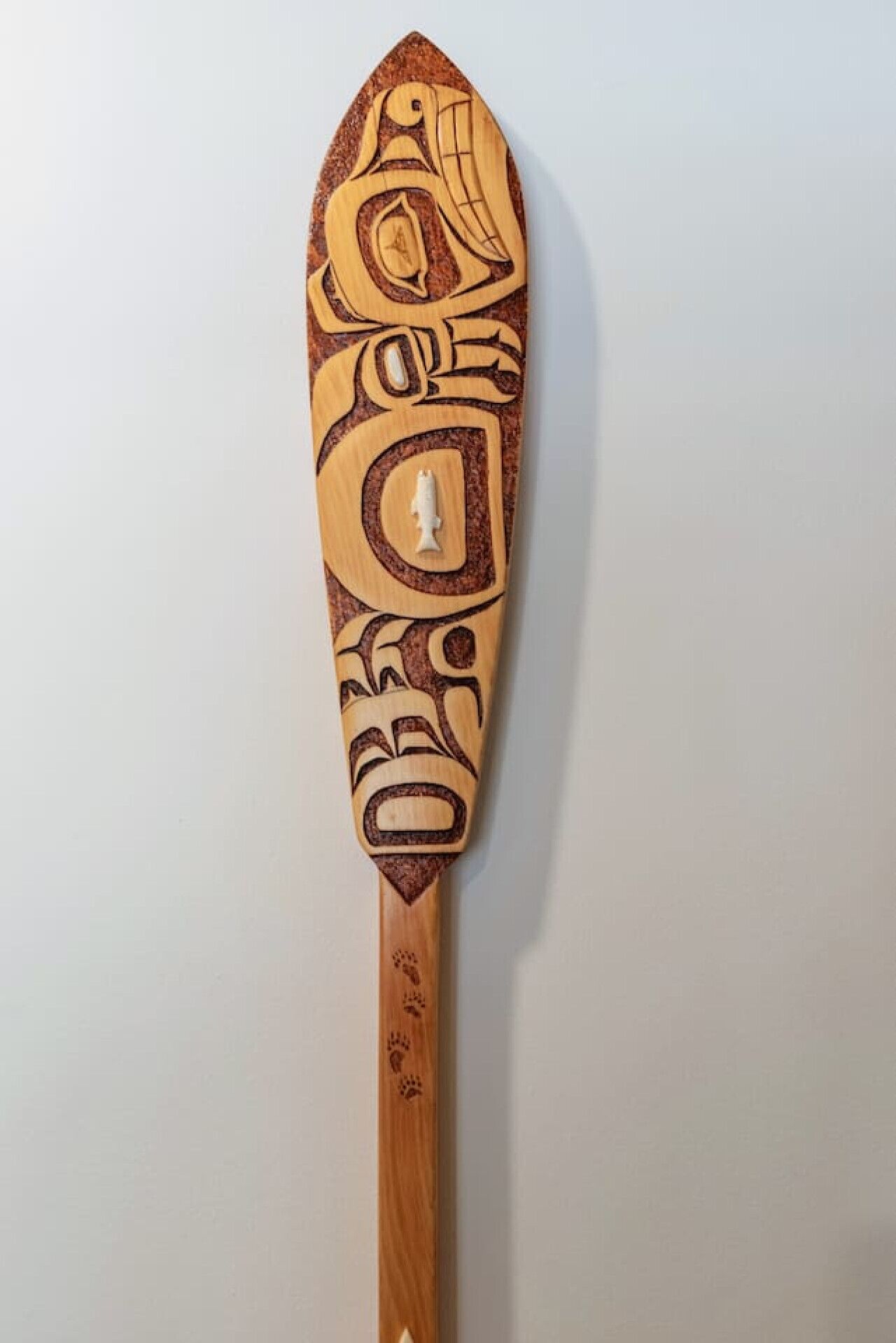 Une pagaie en bois ornée de sculptures complexes et dotée d’un manche lisse.