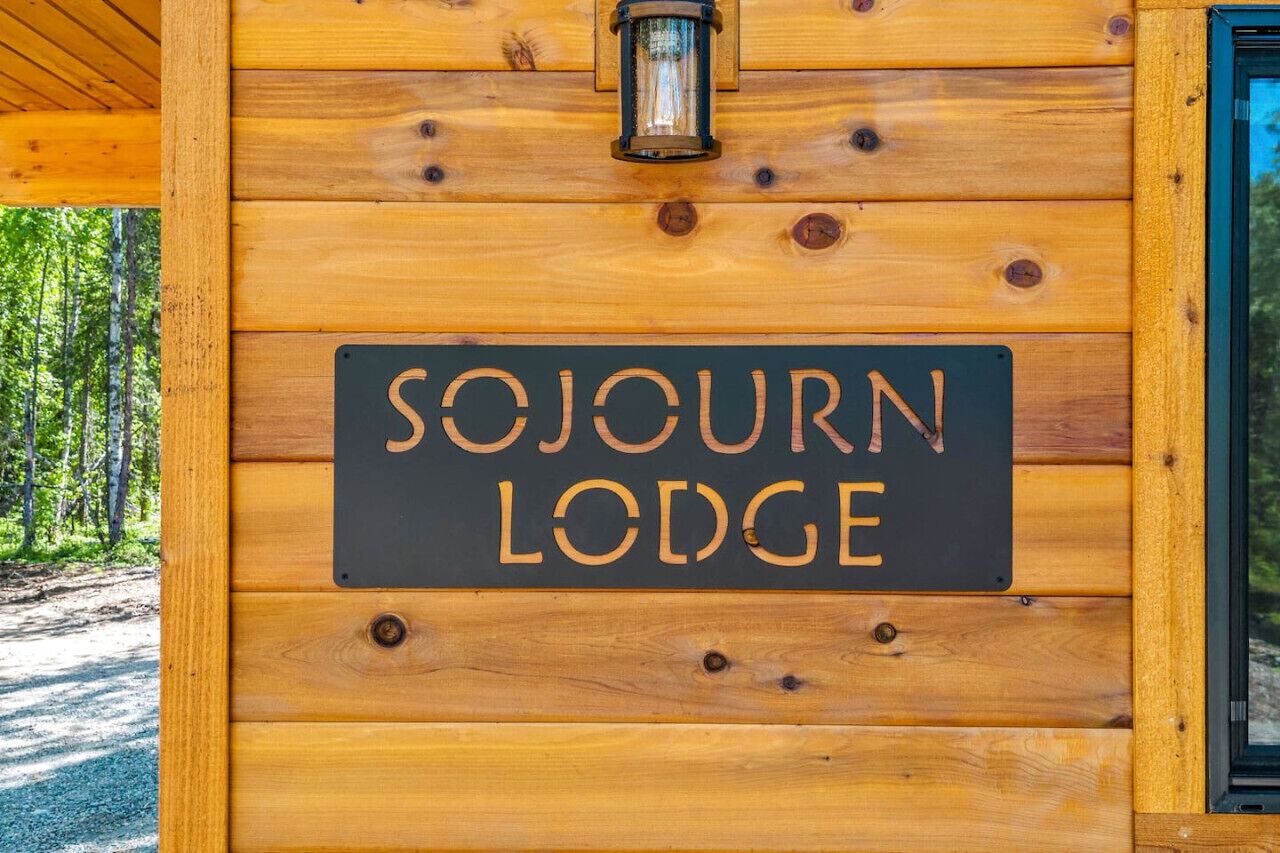 Une enseigne en bois portant l’inscription « SOJOURN LODGE » est fixée à un mur en bois.