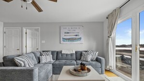 A modern living room with a grey sectional sofa, a coffee table, and a large window with a view of the outdoors. - Charming 2-bedroom Lake House Directly on Cross Lake (Salem Lakes)