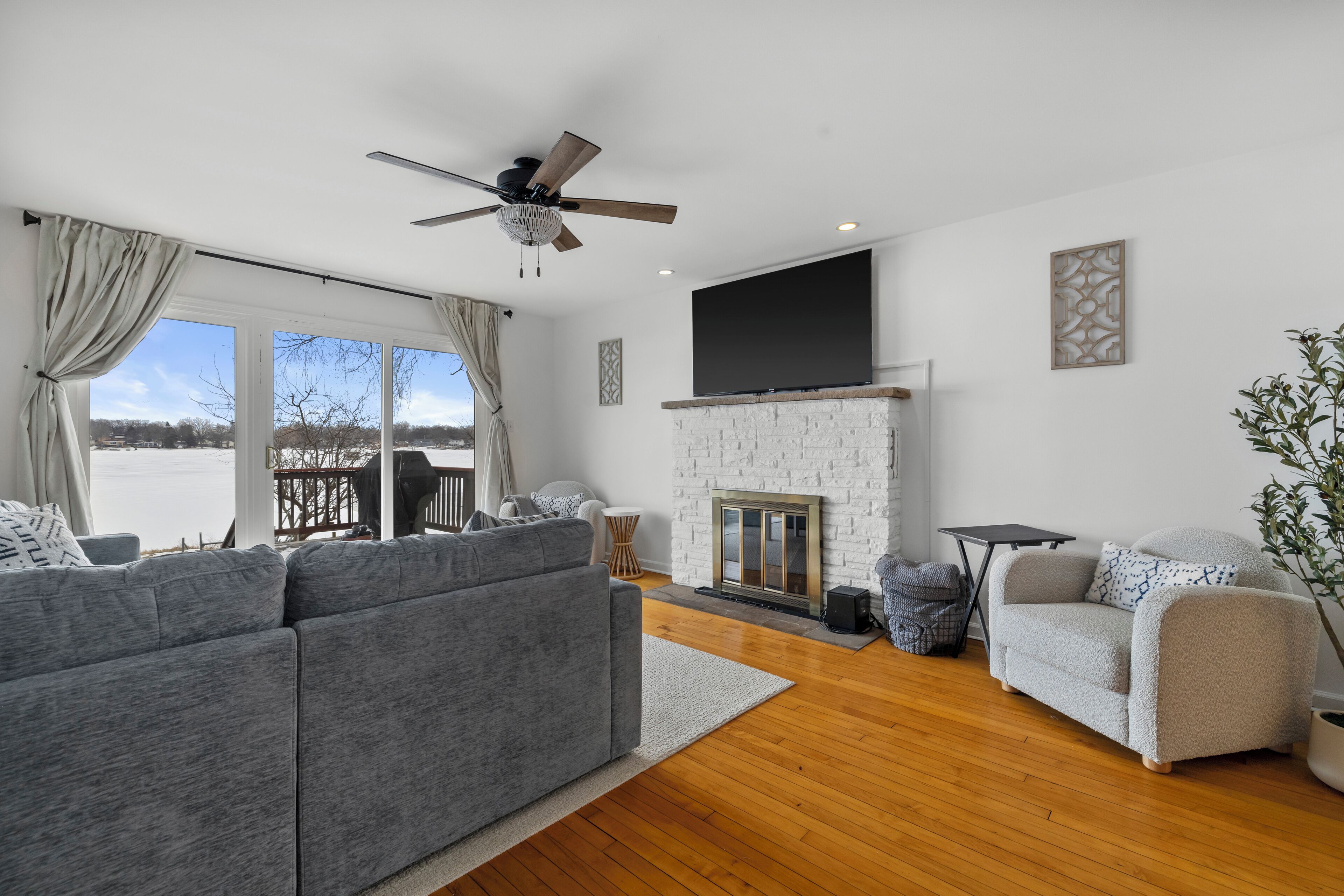 A modern living room with a grey sofa, a white armchair, a fireplace, and a large TV mounted on the wall.
