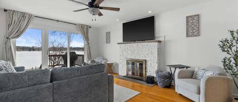 A modern living room with a grey sofa, a white armchair, a fireplace, and a large TV mounted on the wall.