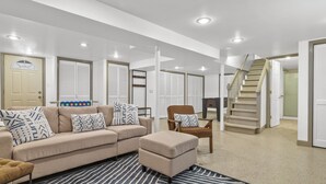 A modern living room with a beige sofa, patterned cushions, a striped rug, and a staircase leading to another level. - Charming 2-bedroom Lake House Directly on Cross Lake (Salem Lakes)