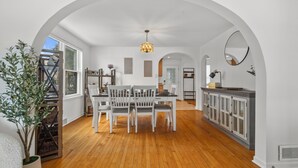 A spacious dining area with a wooden floor, white furniture, and a chandelier. - Charming 2-bedroom Lake House Directly on Cross Lake (Salem Lakes)