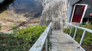 Een houten trap die leidt naar een steiger, met een klein tuinhuisje bovenop.