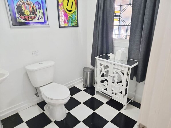 A bathroom with a black and white checkered floor, a white toilet, a white cabinet, and two framed pictures on the wall.
