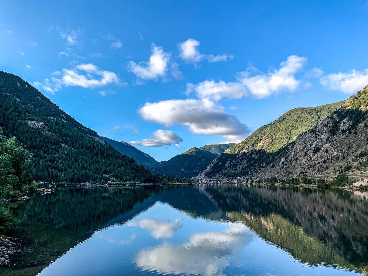Un llac tranquil envoltat de muntanyes boscoses sota un cel serè.