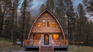 A cabin with a stone foundation, wooden upper walls, and a wooden deck with a railing.