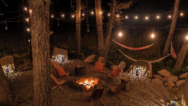 Un área de estar al aire libre con una chimenea, luces colgantes y hamacas.