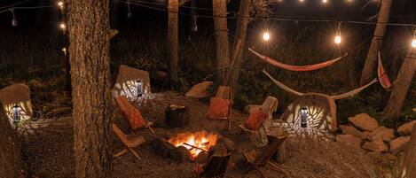 An outdoor seating area with a fire pit, string lights, and hammocks.