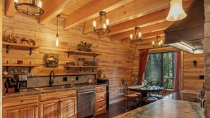 Interior de una cabaña de madera con cocina, comedor y un amplio ventanal.