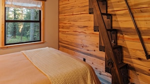 Un interior de madera con una cama, una ventana y una escalera de madera.