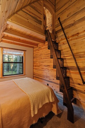 Un interno in legno con un letto, una finestra e una scala in legno.