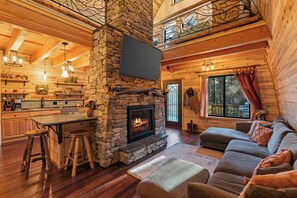 A cozy cabin interior with a stone fireplace, wooden floors, a dining area, and a living room with a sofa. - Your Storybook dream stay for Yellowstone and Grand Teton parks (Island Park)