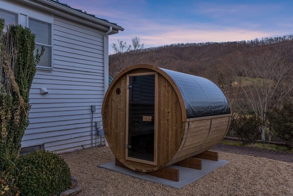 A wooden sauna structure with a door, placed on a gravel surface near a house.