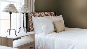 A neatly made bed with white linens, a wooden nightstand with two lamps, and a floral-patterned headboard. - Branch and Barrel: Hot Tub & Sauna + Mtn Views (Roseland)