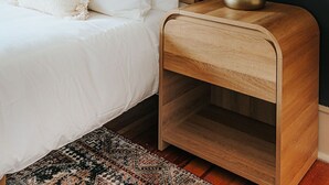 Un dormitorio con cama, una mesita de noche con lámpara y una pared oscura.