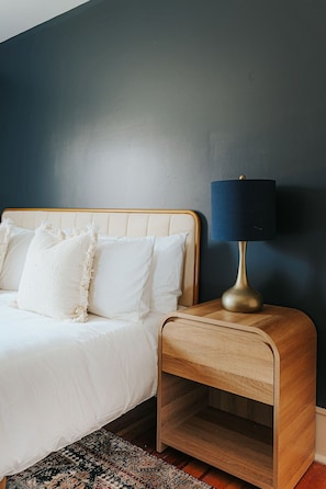 A bedroom with a bed, a bedside table with a lamp, and a dark wall.