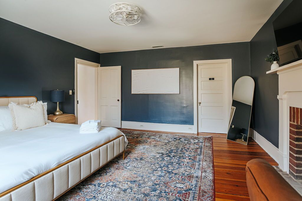 A bedroom with a large bed, a nightstand, a lamp, a rug, and a mirror.