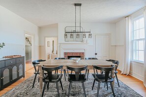 A spacious dining area with a large wooden table, black chairs, and a modern chandelier.