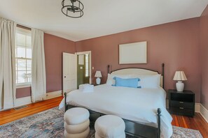 A bedroom with a large bed, two bedside tables with lamps, a door, and a window with curtains.