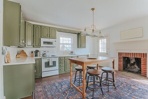 Una cocina con gabinetes verdes, una mesa de madera con taburetes, una chimenea y un tapete estampado.