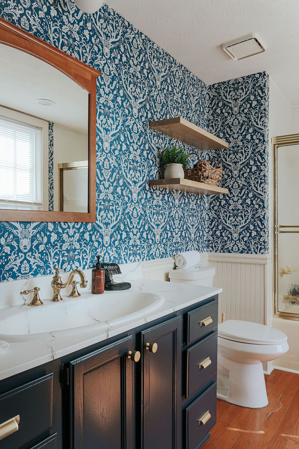 A bathroom with a white sink, dark cabinets, a white toilet, and blue patterned wallpaper.