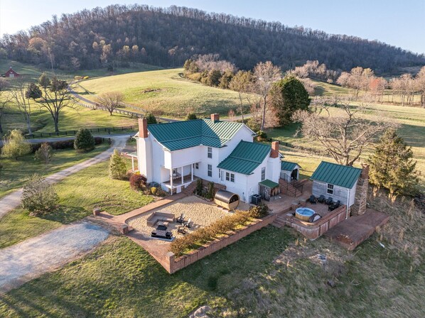A large white house with a green roof, a patio with outdoor furniture, and a swimming pool.