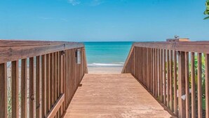 Een houten pad dat naar een strand leidt, onder een heldere blauwe lucht.