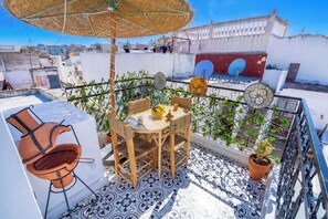 A rooftop terrace with a table and chairs, a grill, and potted plants.