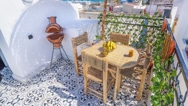 Een terras op het dak met een tafel, stoelen, een hangende plant en uitzicht op de stad.