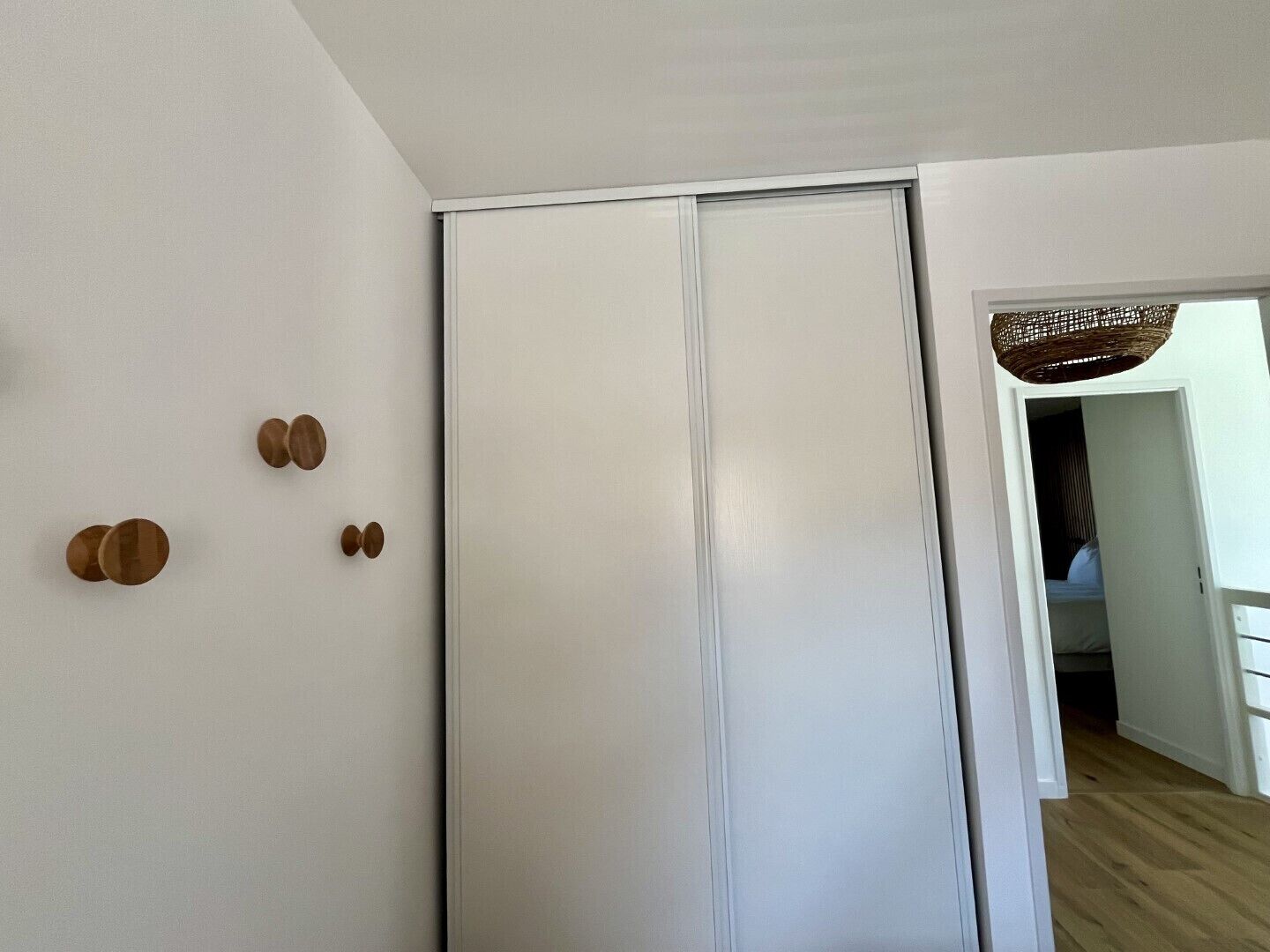 Une pièce avec une armoire blanche, un panier en osier suspendu au plafond et un plancher en bois.