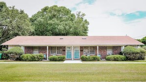 A single-story brick house with a front porch, a central door, and a small attached garage. - 3-bedroom, 2-bathroom beach getaway Tranquil Waves, Jekyll Island (Jekyll Island)
