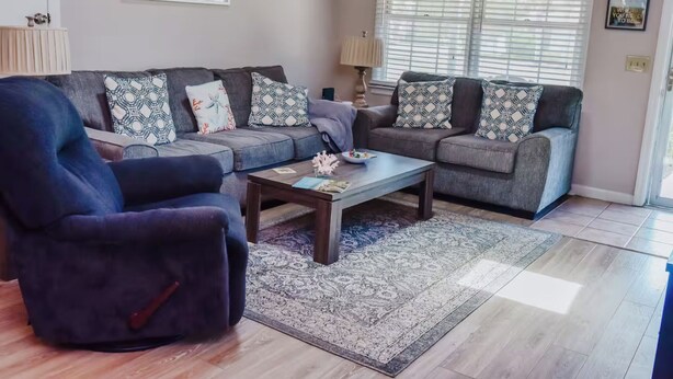 A living room with a grey sofa set, a blue armchair, a wooden coffee table, and patterned cushions. - 3-bedroom, 2-bathroom beach getaway Tranquil Waves, Jekyll Island (Jekyll Island)
