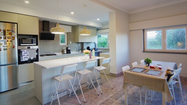 Una cocina moderna con una isla central, sillas blancas y una mesa de comedor con vistas al exterior.