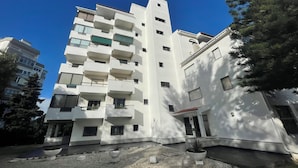 Un edificio residencial de varios pisos con balcones, un patio empedrado y árboles circundantes.