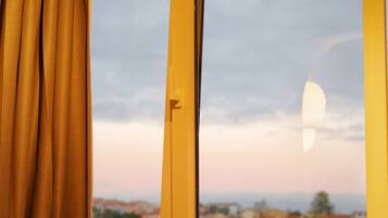 A window with a view of a town, curtains, and a partially visible moon.