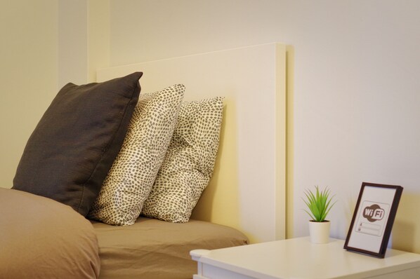 Una cama con dos almohadas, una planta pequeña en maceta y un cuadro en la mesita de noche.
