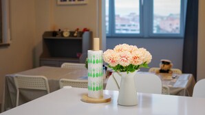 Un comedor con una mesa dispuesta para dos personas, un jarrón con flores y un dispensador decorativo para toallas de papel.