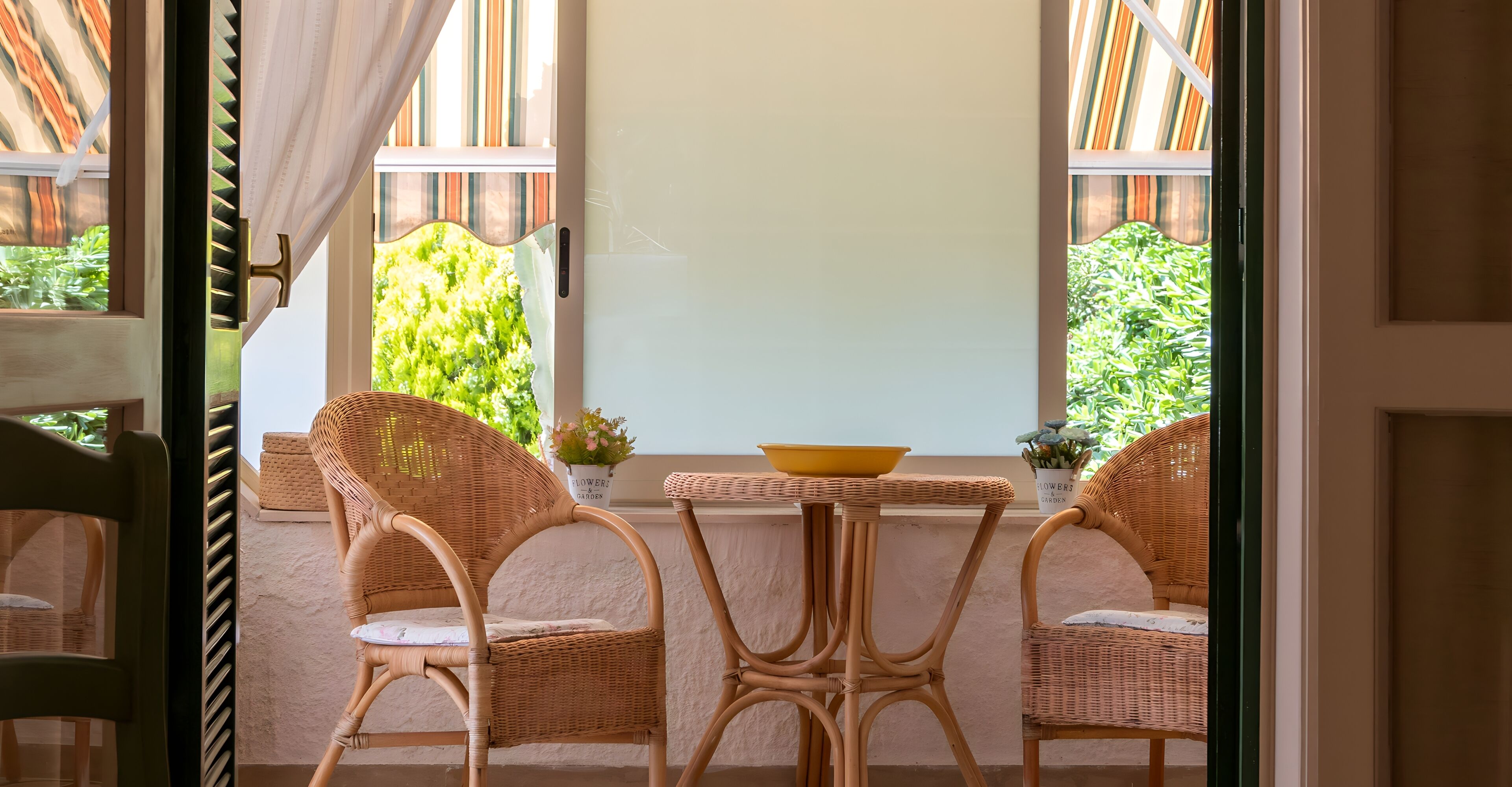 A room with wicker furniture, a yellow bowl on a table, and a view of greenery outside.