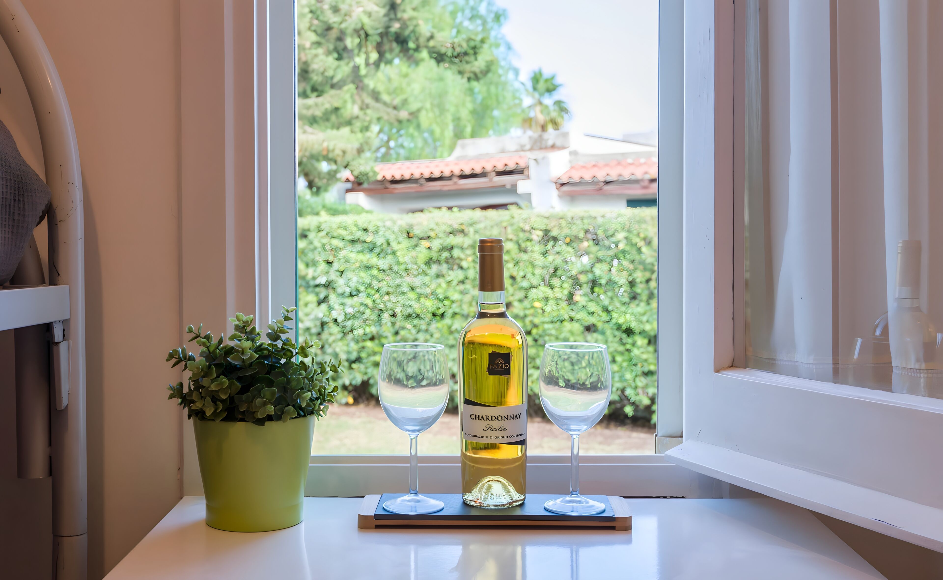Eine Flasche Chardonnay und zwei Gläser auf einem Fensterbrett mit einer Topfpflanze.