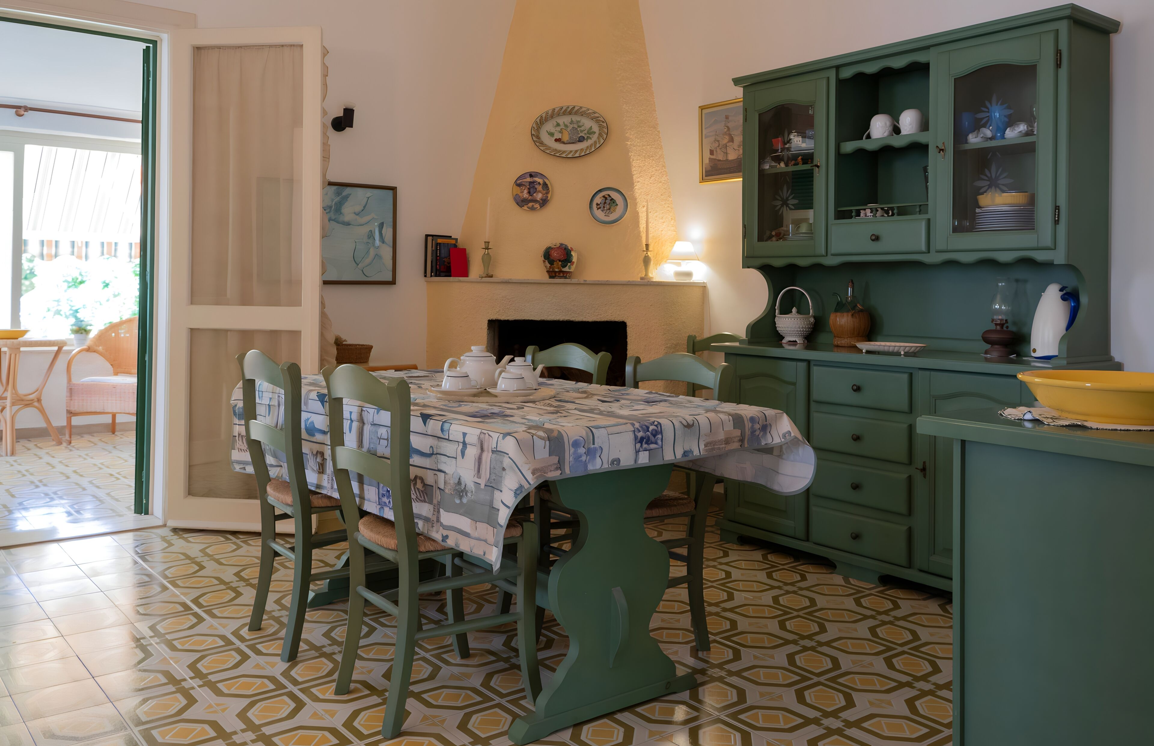 A dining area with a table set for four, chairs, a green cabinet with dishes, and a fireplace.