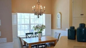A dining area with a wooden table, chairs, and a chandelier. There is a window with blinds and a clock on the wall. - Gorgeous Paradise Village boating community on the Imperial River (Bonita Springs)