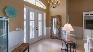 A spacious living room with a high ceiling, a chandelier, a large mirror, and a television. - Gorgeous Paradise Village boating community on the Imperial River (Bonita Springs)