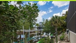 A wooden dock leading to a glass bridge over water, surrounded by lush greenery and a clear sky. - Gorgeous Paradise Village boating community on the Imperial River (Bonita Springs)