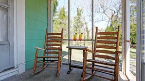 A porch with two rocking chairs and a small table, a green wall, and a window with a view of trees. - Charming 3-bedroom farmhouse with AC, WiFi,  5 minutes to Sea Isle Beaches! (Dennis)