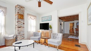 A living room with a brick accent wall, two armchairs, a coffee table, and a TV. - Charming 3-bedroom farmhouse with AC, WiFi,  5 minutes to Sea Isle Beaches! (Dennis)