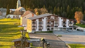 Ein mehrstöckiges Gebäude mit einem zentralen Innenhof, umgeben von einem Parkplatz und einer kleinen Kapelle im Hintergrund.